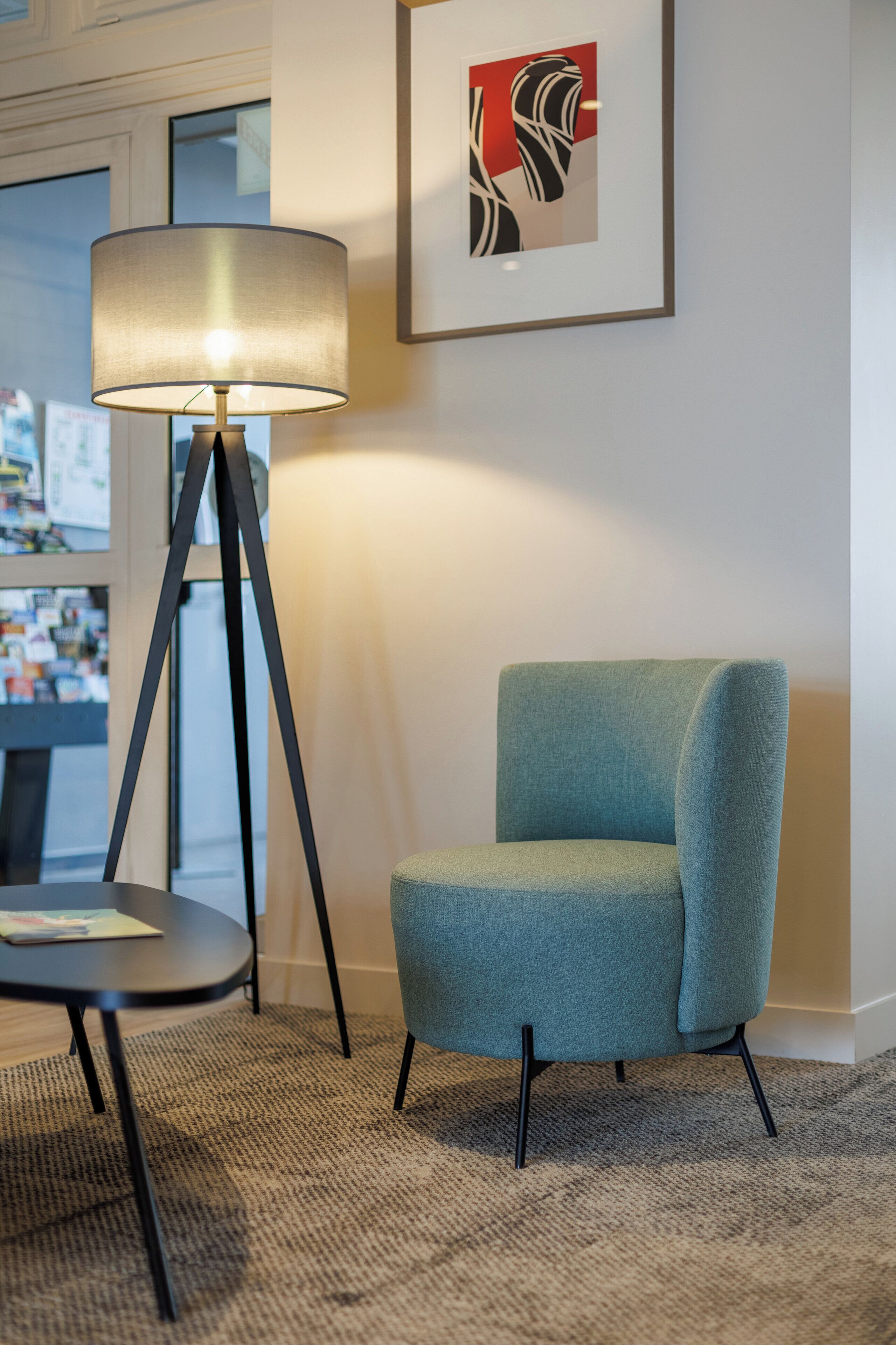 A modern room with a teal armchair, a floor lamp, and a framed abstract artwork on the wall.