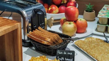 Un buffet de petit-déjeuner proposant des gaufres, des toasts et une variété de fruits, notamment des pommes et des kiwis.