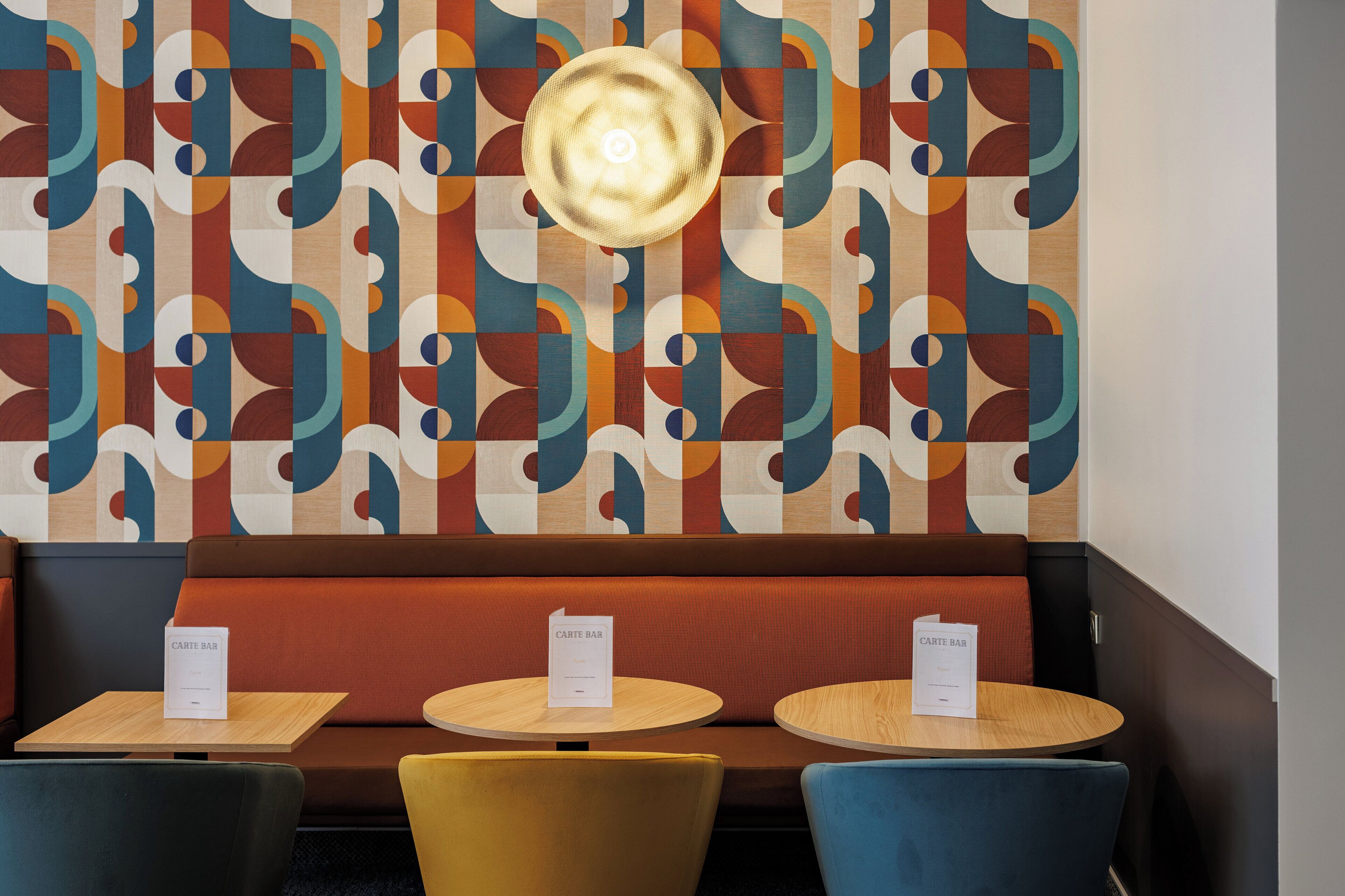 A restaurant interior with a patterned wall, a central light fixture, and seating with 'CARTE BAR' signs.