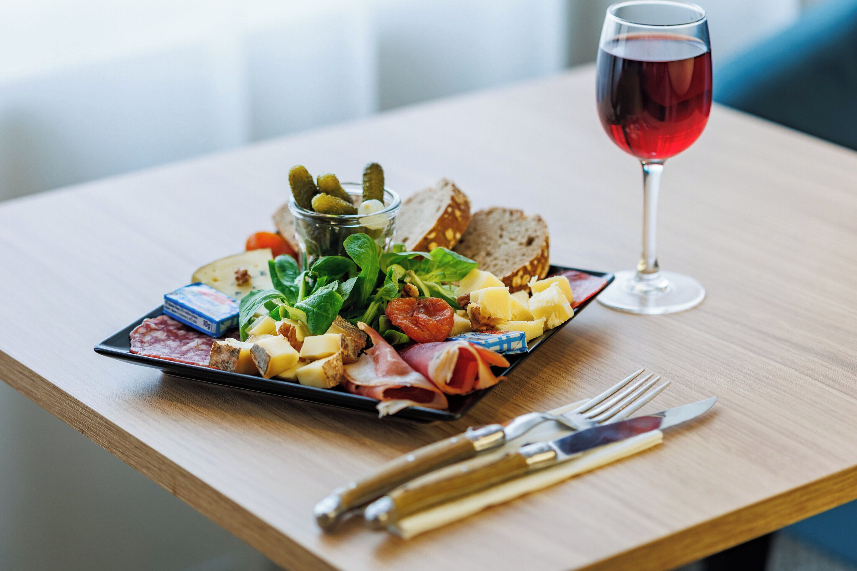A wooden table with a charcuterie board, a glass of red wine, and cutlery.