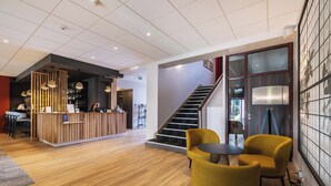A modern reception area with a wooden desk, a staircase, and yellow chairs. - The Originals Boutique, Hôtel Le Pariou (Issoire)