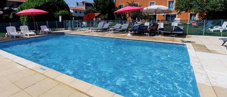 Una piscina con sillas de descanso y sombrillas, rodeada de edificios.
