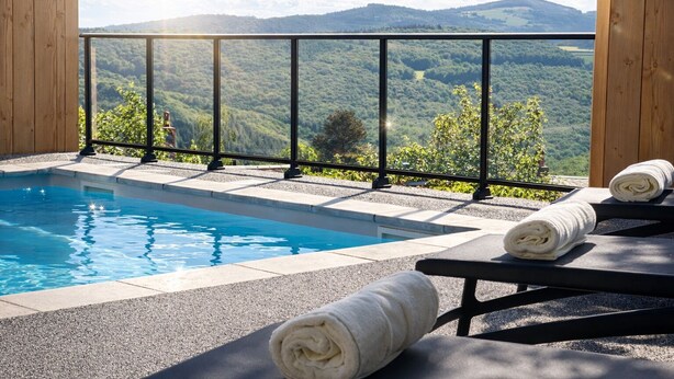 Piscina con vista a las montañas, muelle de madera y sillas de descanso con toallas.