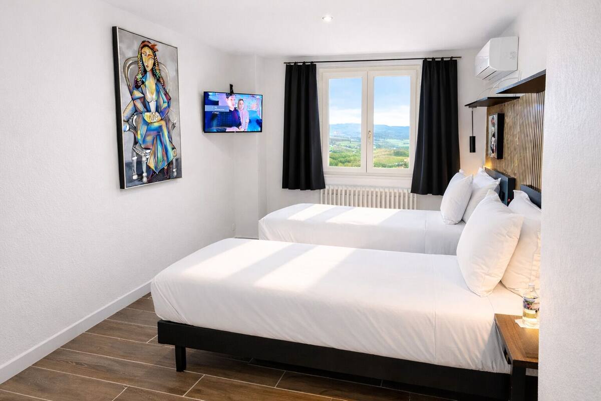 Ein Hotelzimmer mit zwei Betten, einem Fernseher, einem Gemälde und einem Fenster mit Blick.
