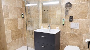 Un baño con cabina de ducha de vidrio, un lavabo con espejo, un inodoro y un calentador de pared.