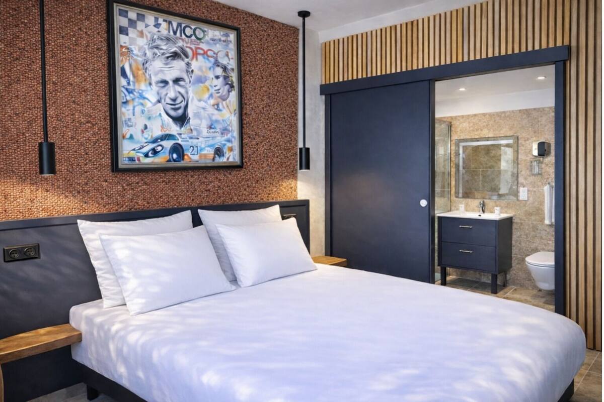 Ein modernes Hotelzimmer mit einem großen Bett, einem Holzkopfende, einem gerahmten Poster an der Wand und einer Schiebetür zum Badezimmer.