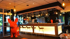 A bar area with a counter, stools, and a large red sculpture. - Kyriad Clermont Ferrand Nord - Riom (Riom)