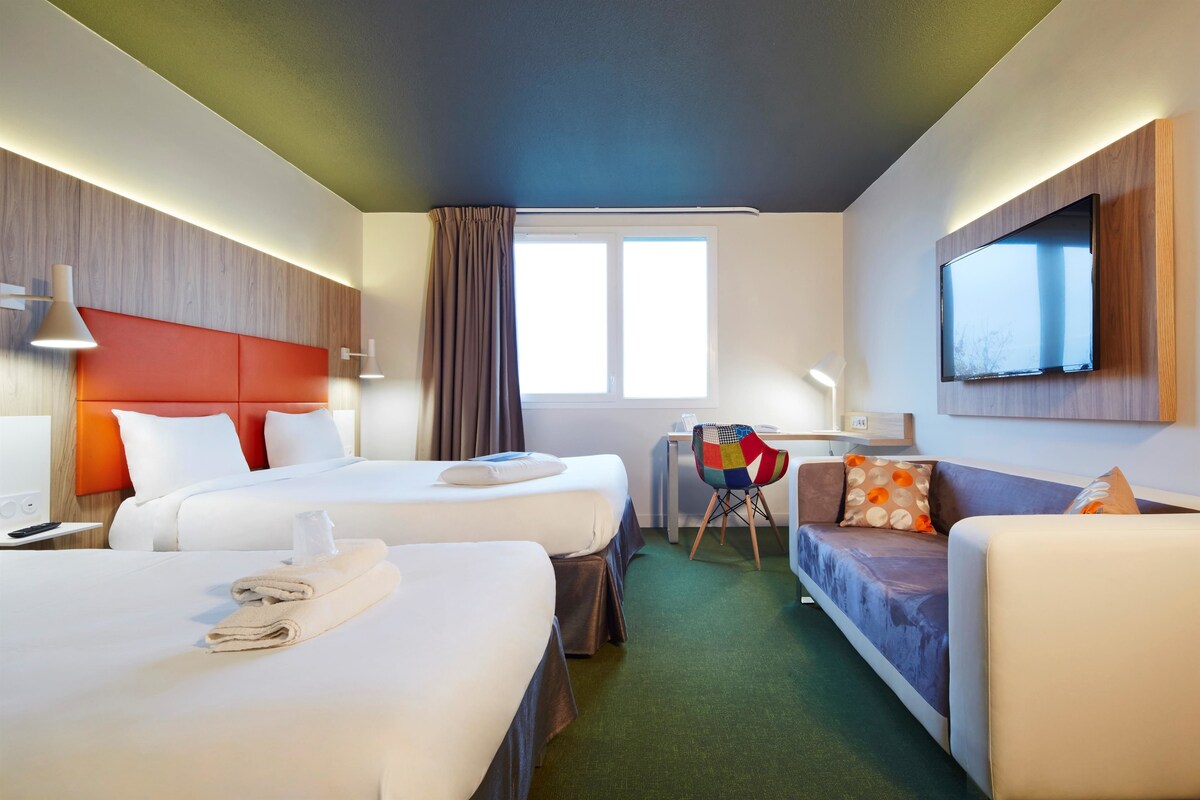 Una habitación de hotel con dos camas, un escritorio, una silla, un sofá, un televisor y una ventana.
