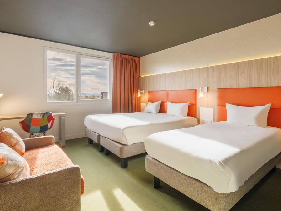Une chambre d’hôtel avec deux lits, un bureau, une chaise et une fenêtre donnant sur un paysage agréable.