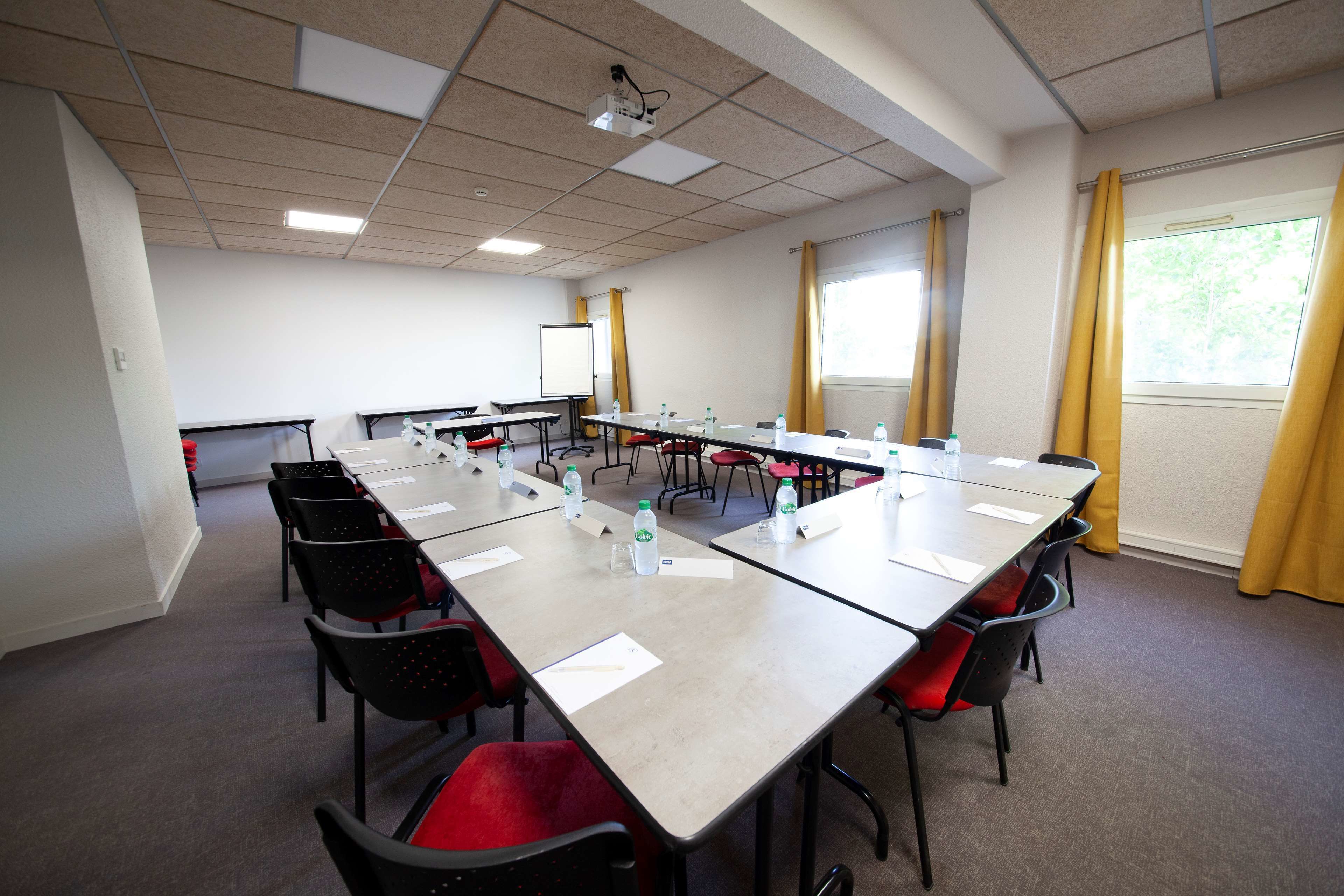 A conference room with a long table, black chairs, red cushions, water bottles, and a whiteboard.