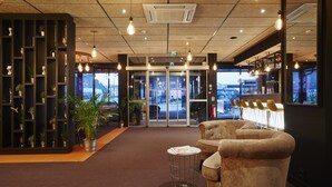A lobby with a central seating area, a reception desk, and a view of the street outside. - Kyriad Clermont Ferrand Nord - Riom (Riom)