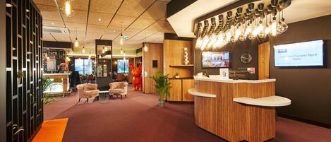 A reception area with a wooden reception desk, multiple light fixtures, and a digital screen displaying room information.