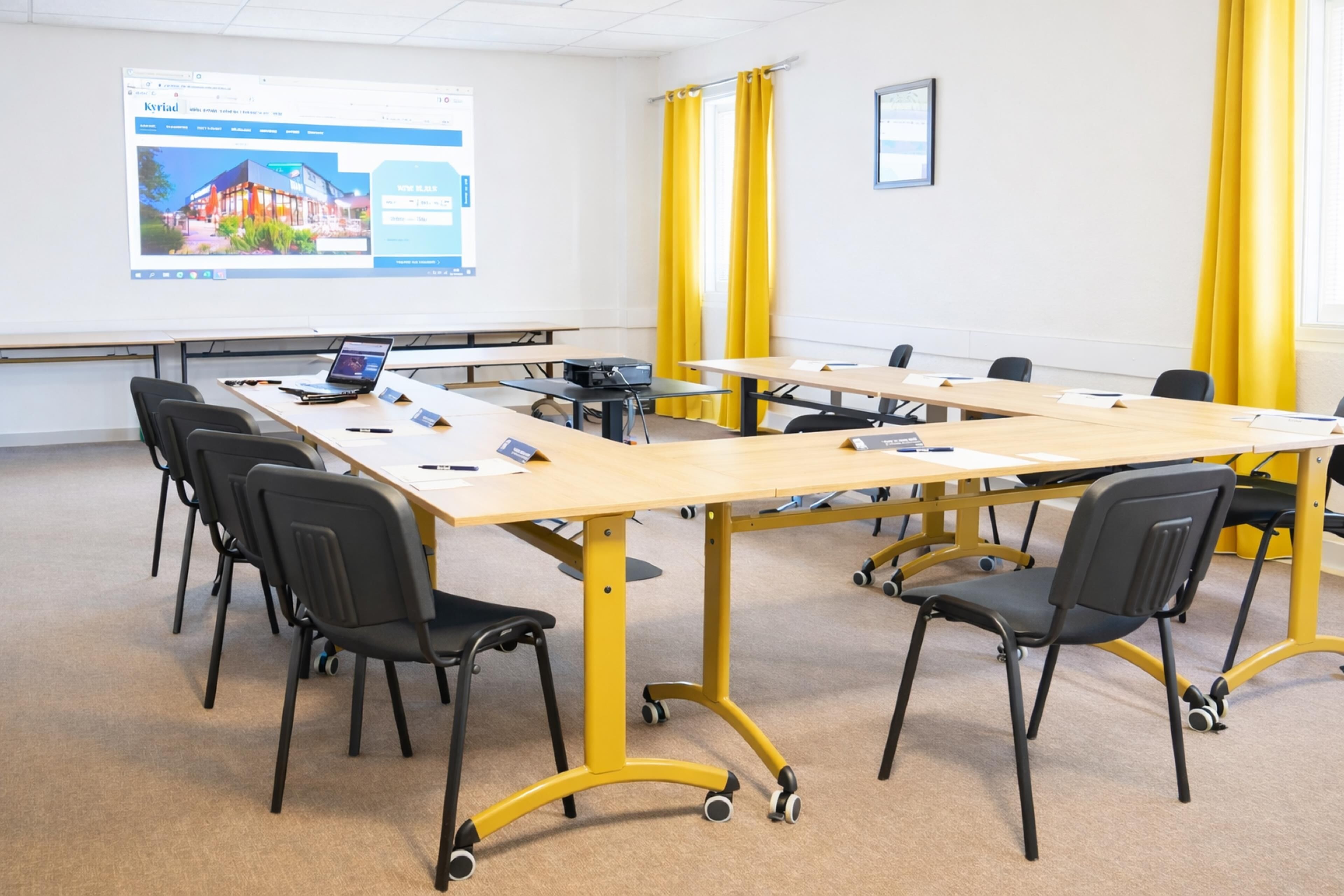 Une salle de conférence équipée d’une grande table, de chaises, d’un ordinateur portable et d’un écran de présentation.