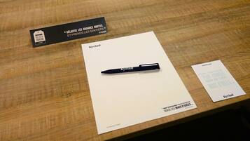 Una mesa de madera con una etiqueta negra, una tarjeta blanca con la palabra 'Kyriad' y un bolígrafo, además de una pequeña tarjeta con texto.