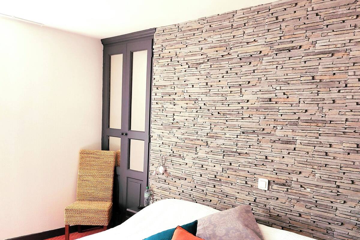 A bed with a patterned headboard, a wicker chair, and a door with a dark frame.