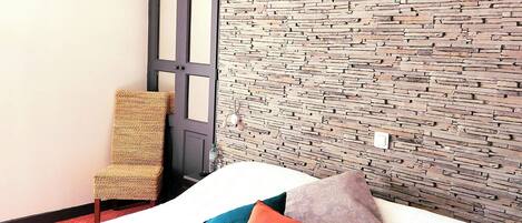 A bed with a patterned headboard, a wicker chair, and a door with a dark frame.
