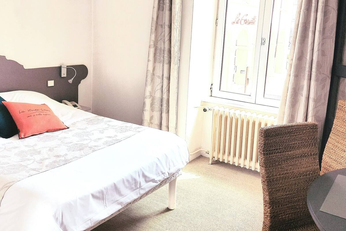 A hotel room with a bed, a chair, a radiator, and curtains.