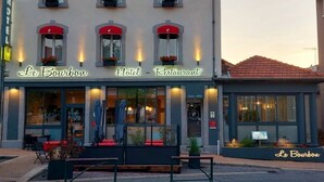 Un hotel con un cartel que dice "Le Bourbon Hotel - Restaurant". Tiene varias ventanas con toldos rojos y mesas al aire libre.