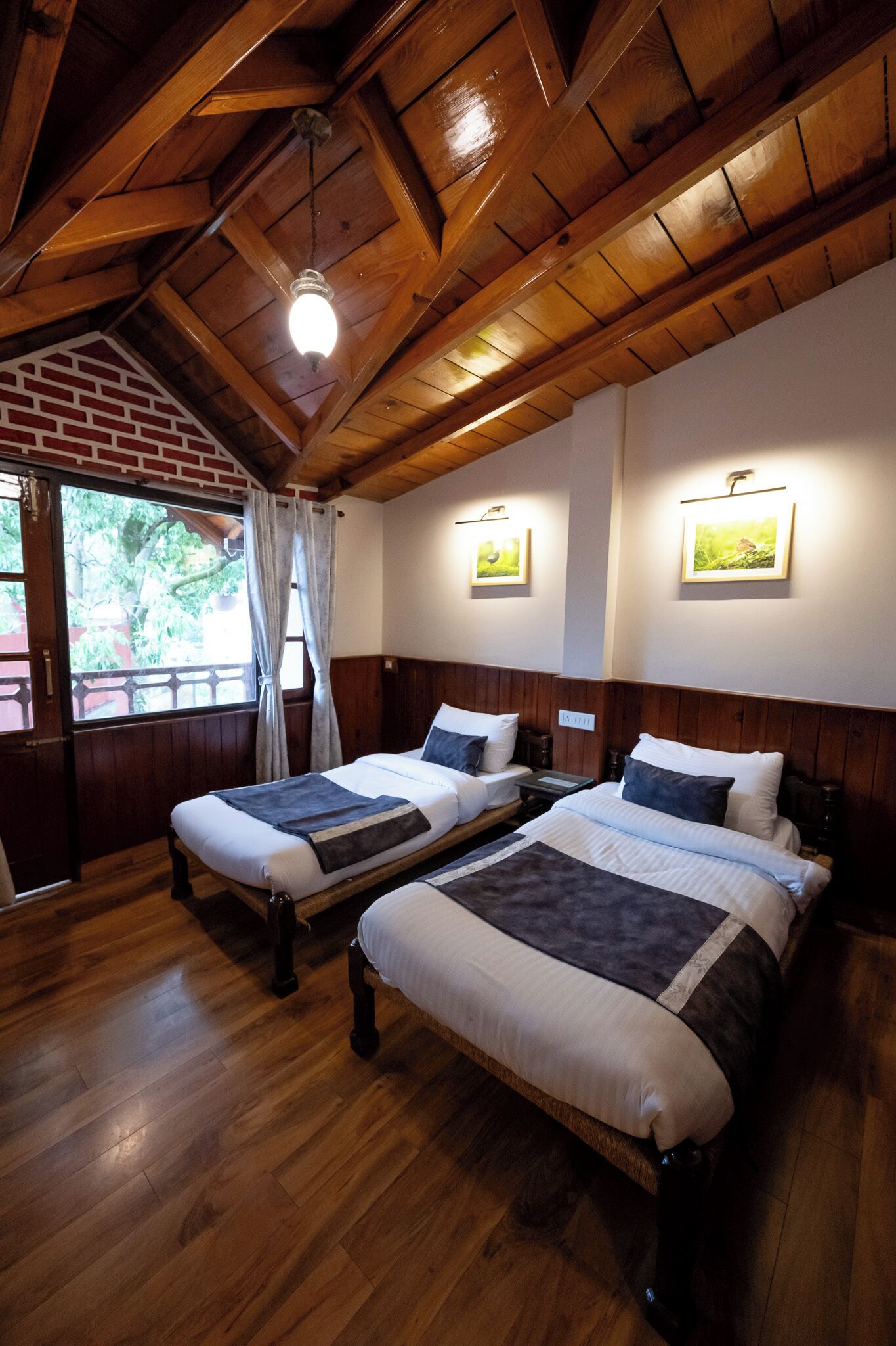 A room with two beds, wooden floors, a sloped ceiling, and framed pictures on the walls.