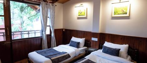 A room with two beds, wooden floors, a sloped ceiling, and framed pictures on the walls.