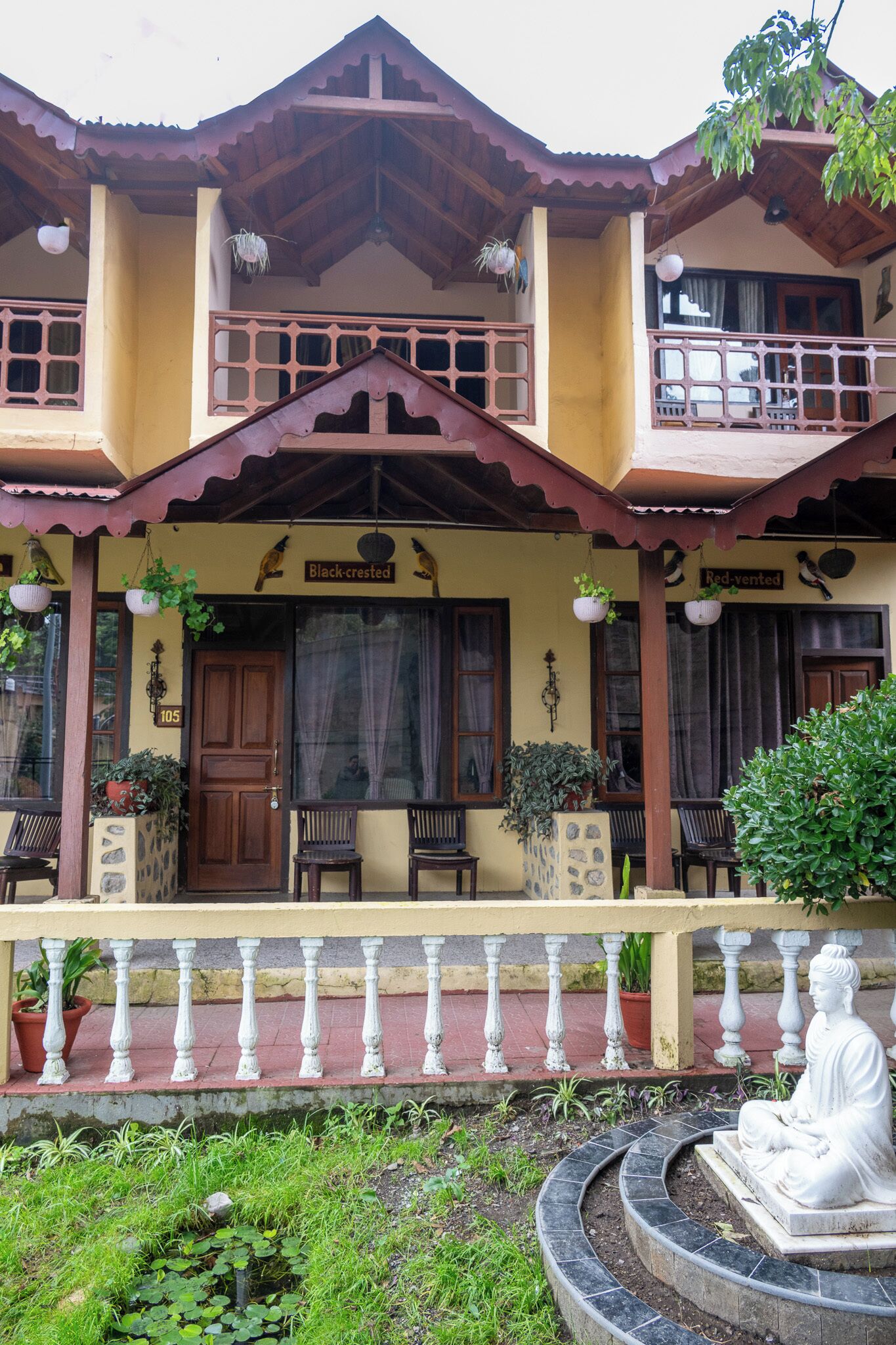 A two-story building with a balcony, a statue, and potted plants.
