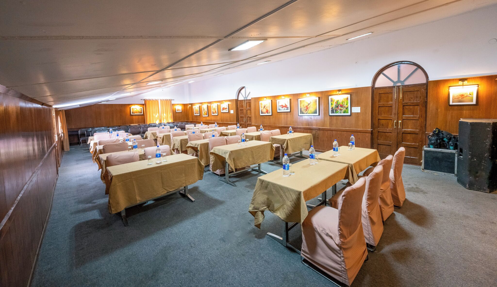 Una sala de conferències amb diverses taules i cadires, equipada amb ampolles d'aigua i decorada amb quadres a les parets.