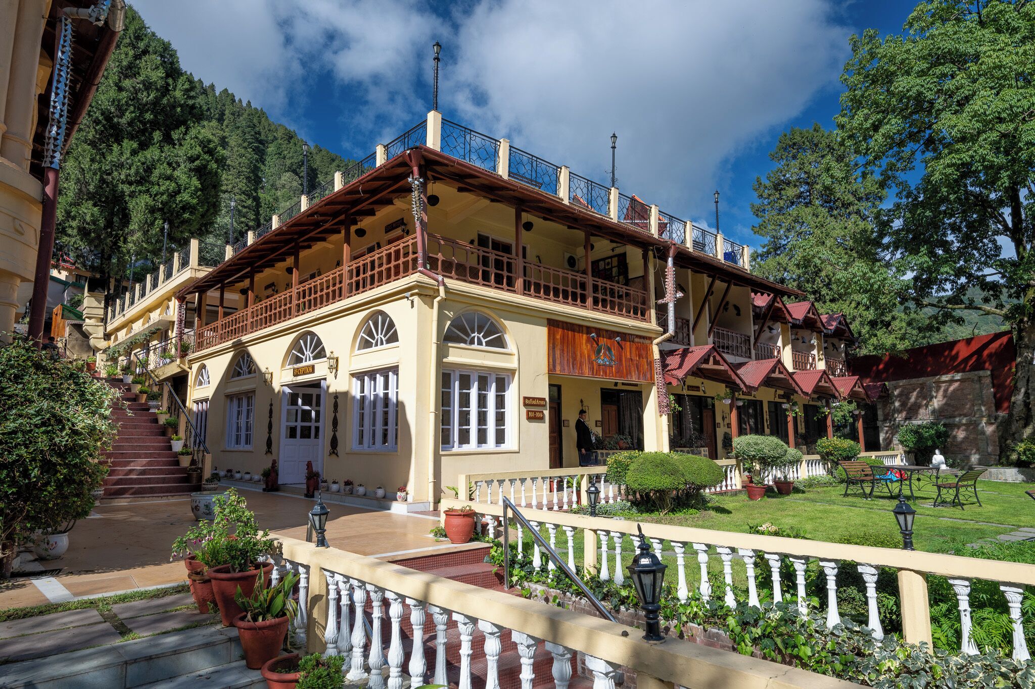 A two-story building with a balcony, a staircase leading to the entrance, and a well-maintained garden area.