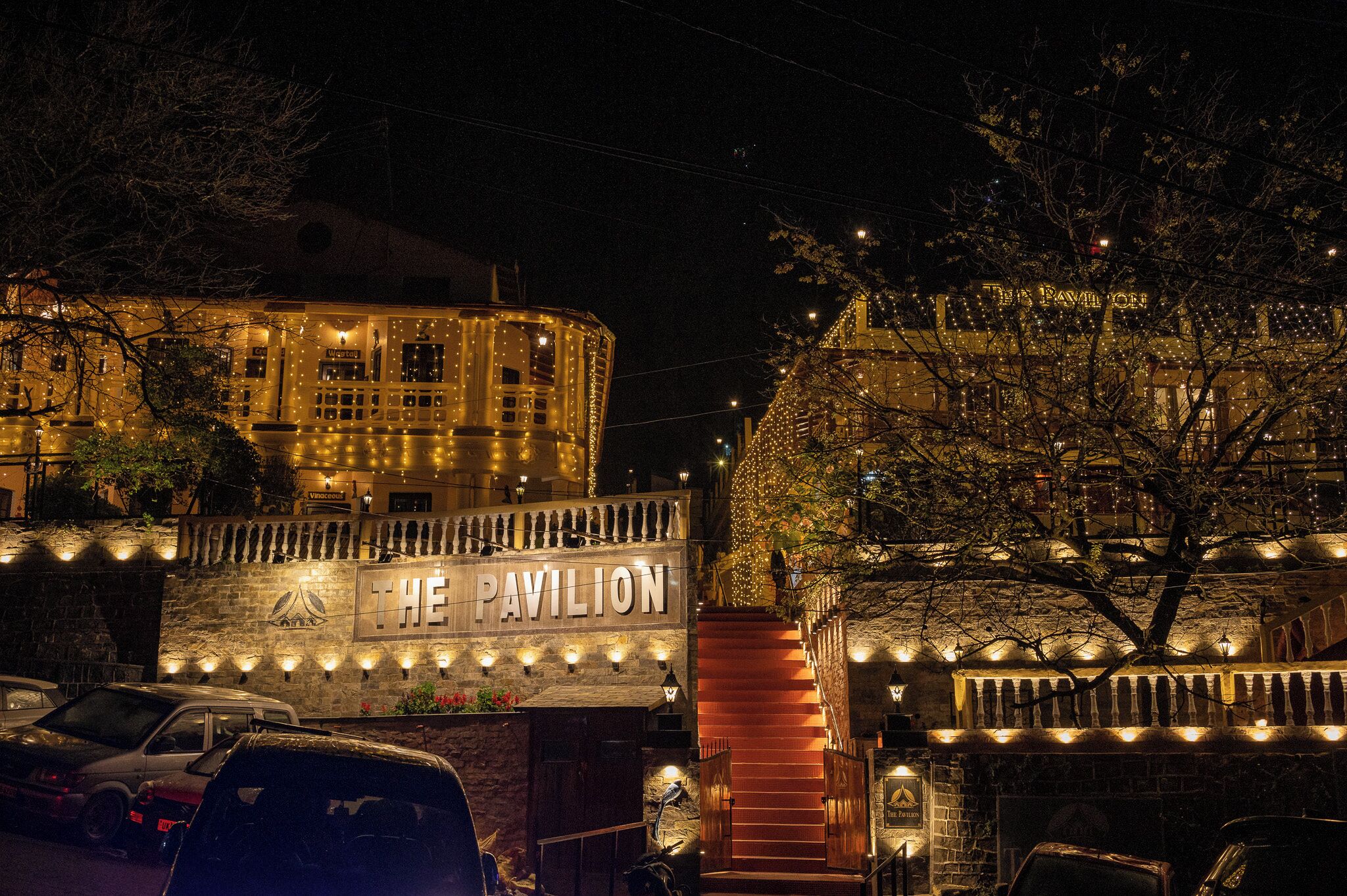 Un edificio con un cartel que dice "The Pavilion" de noche, con ventanas iluminadas y una escalera.