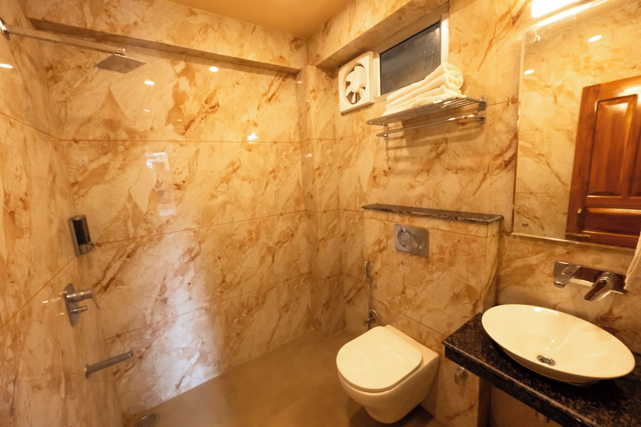 Een badkamer met marmeren wanden, een toilet, een bidet, een wastafel en een spiegel.