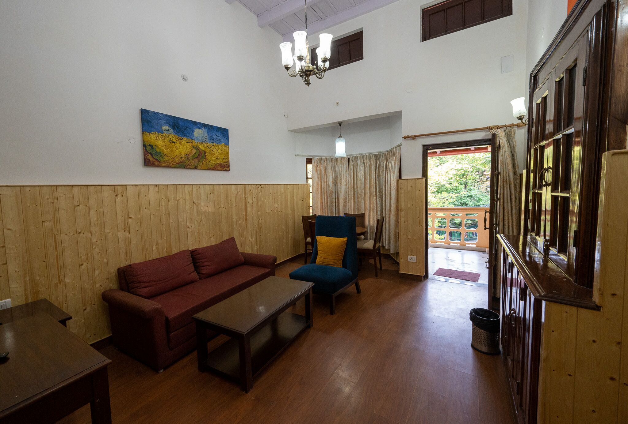 Un vaste espace de vie doté d’un plancher en bois, d’un canapé rouge, d’un fauteuil bleu et d’un tableau accroché au mur.