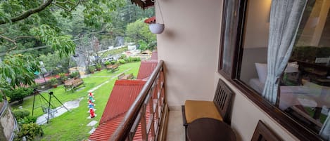 En balkon med udsigt over en have, rødt tag samt et træbord og en stol.