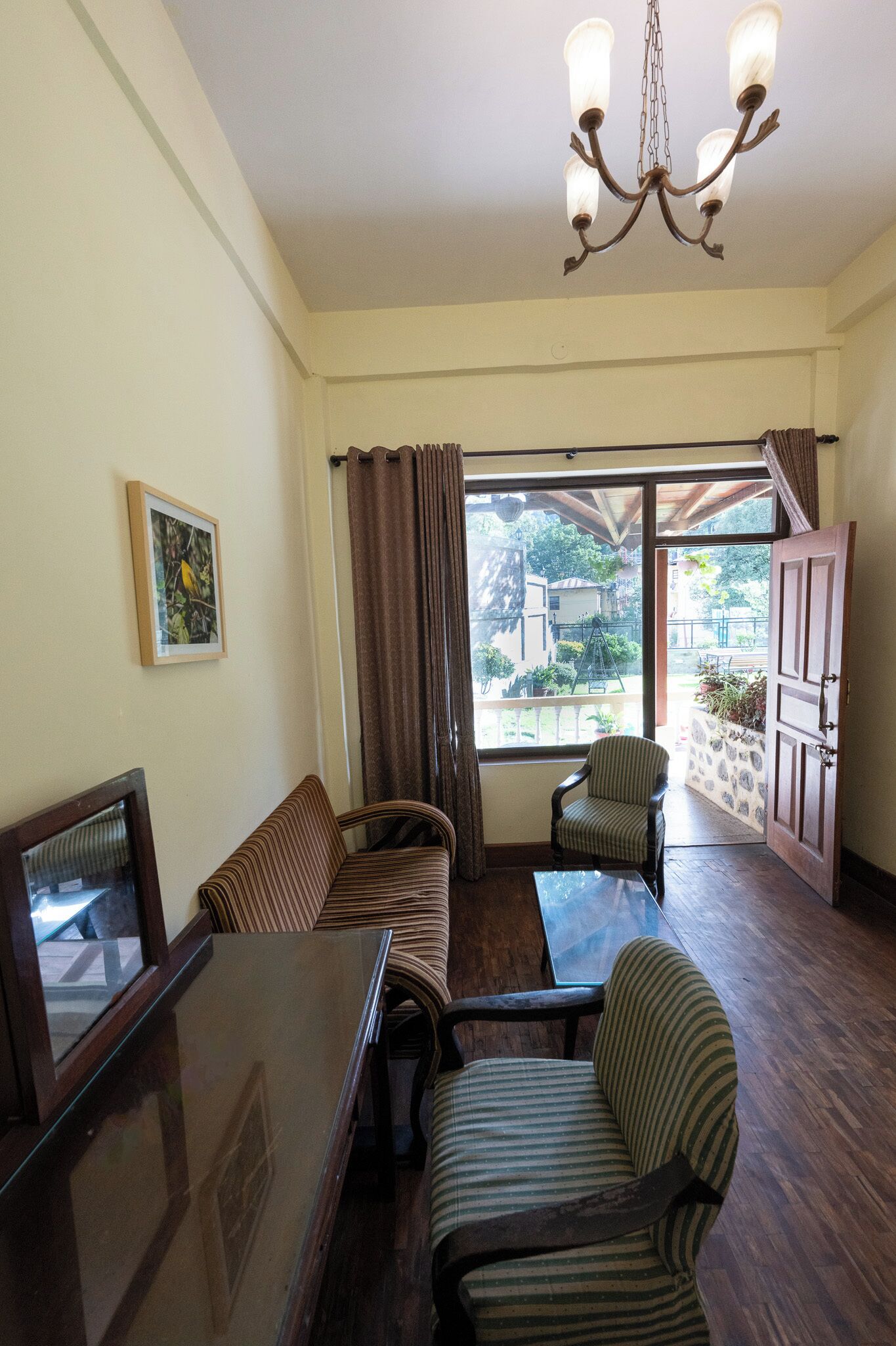 Sala de estar con sofá, sillones, una mesa con cubierta de vidrio, candelabro, un cuadro en la pared y vistas amplias a través de un ventanal.