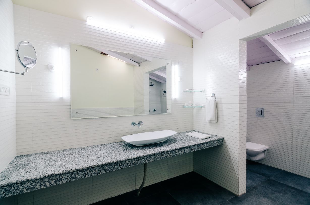 Un bagno moderno con una parete rivestita in piastrelle bianche, un piano di lavoro in granito, un lavandino bianco, uno specchio grande e un water.