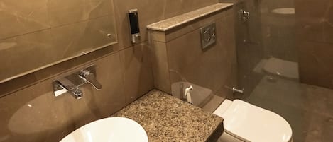 Un baño moderno con encimera de granito, un lavamanos blanco y una ducha con mampara de vidrio.