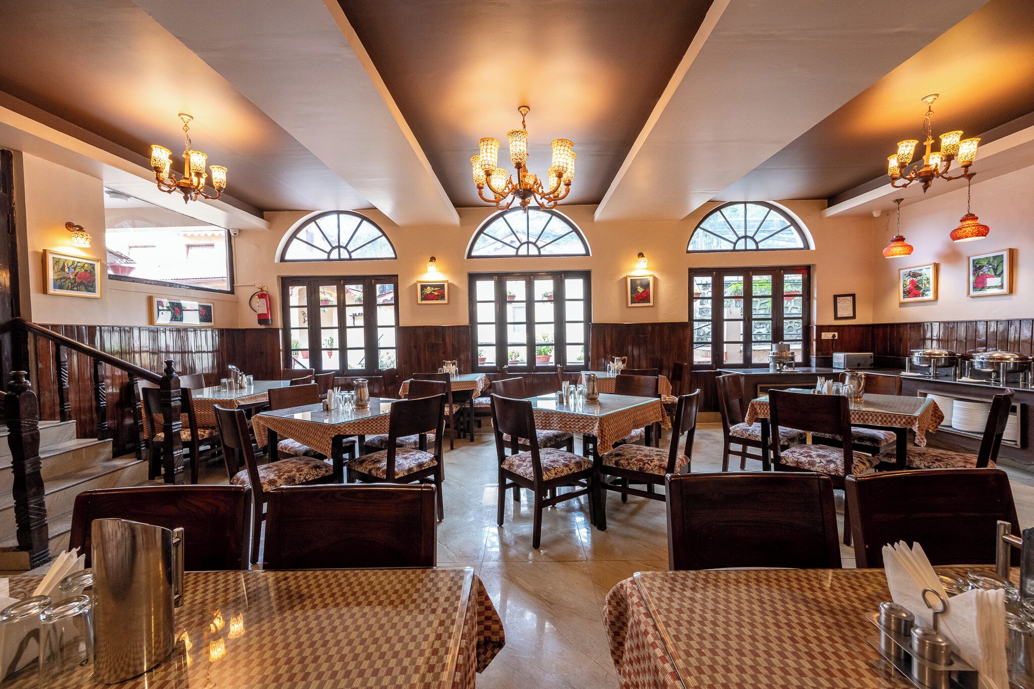 A restaurant with multiple dining tables, chairs, and chandeliers.