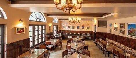 A restaurant with multiple dining tables and booths, a chandelier, and framed artwork on the walls.