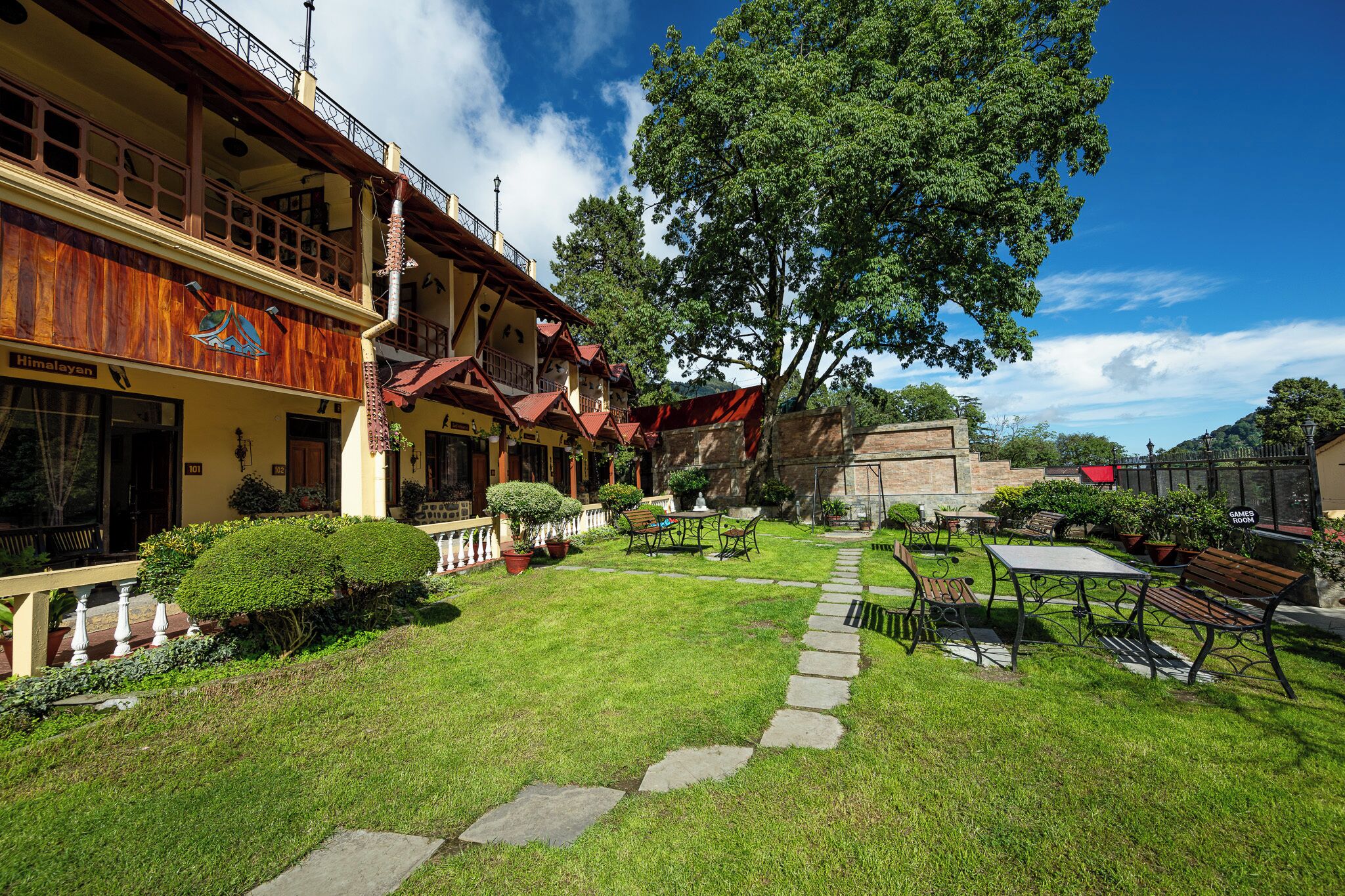 A hotel with a well-maintained garden, outdoor seating, and a large tree providing shade.