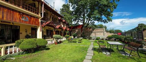 A hotel with a well-maintained garden, outdoor seating, and a large tree providing shade.