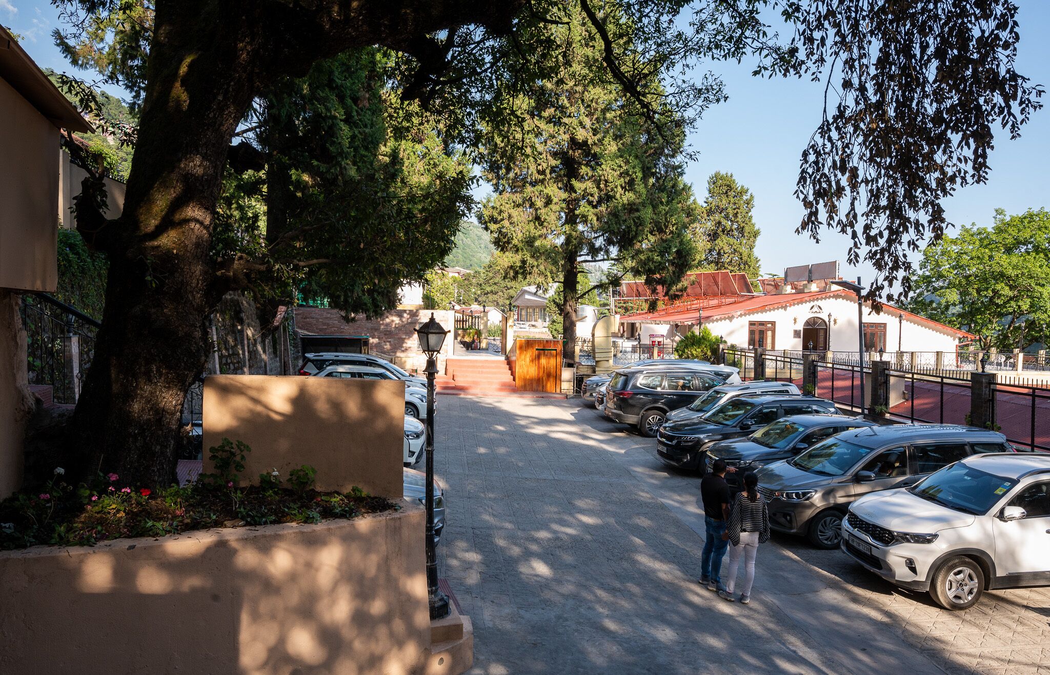 Ein Parkplatz mit mehreren Autos, ein Gebäude mit rotem Dach und eine von Bäumen gesäumte Straße.