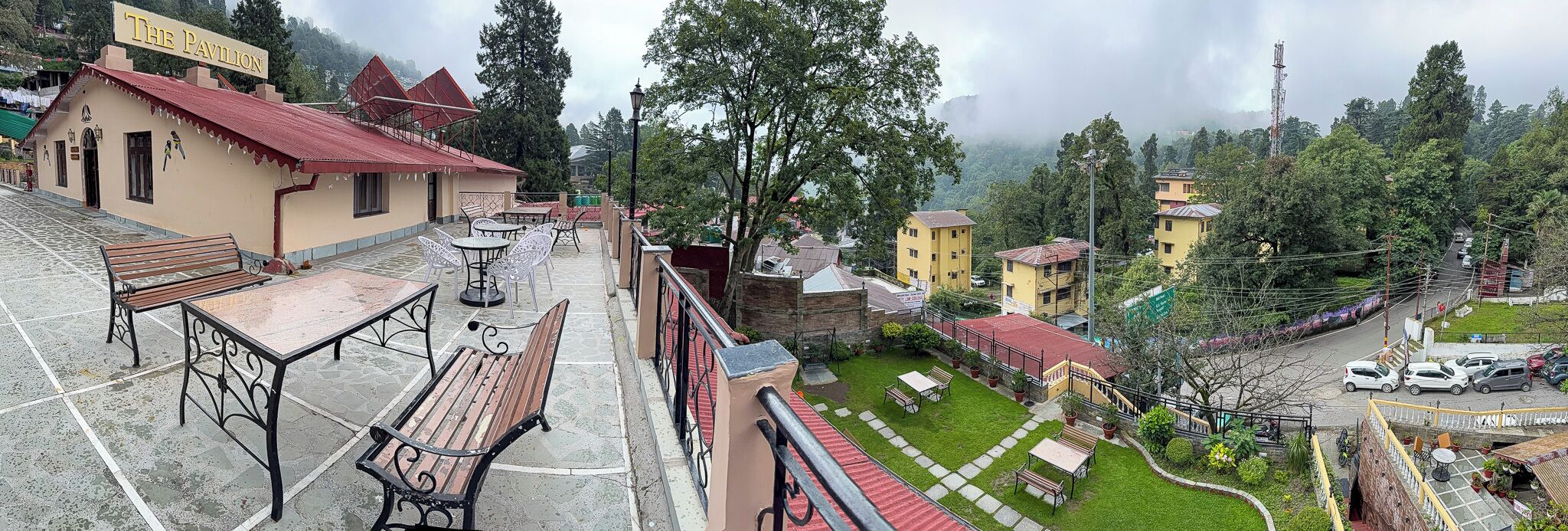 A terrace with outdoor seating, a building labeled "The Pavilion," and a view of a town with houses and greenery.