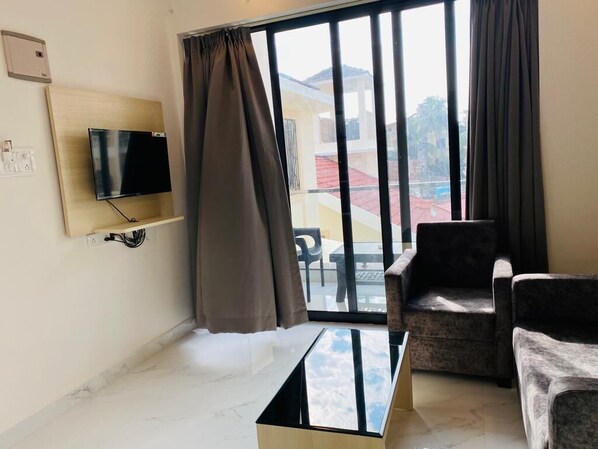 A hotel room with a TV mounted on the wall, a glass table, two chairs, and a view of the outside through large windows.