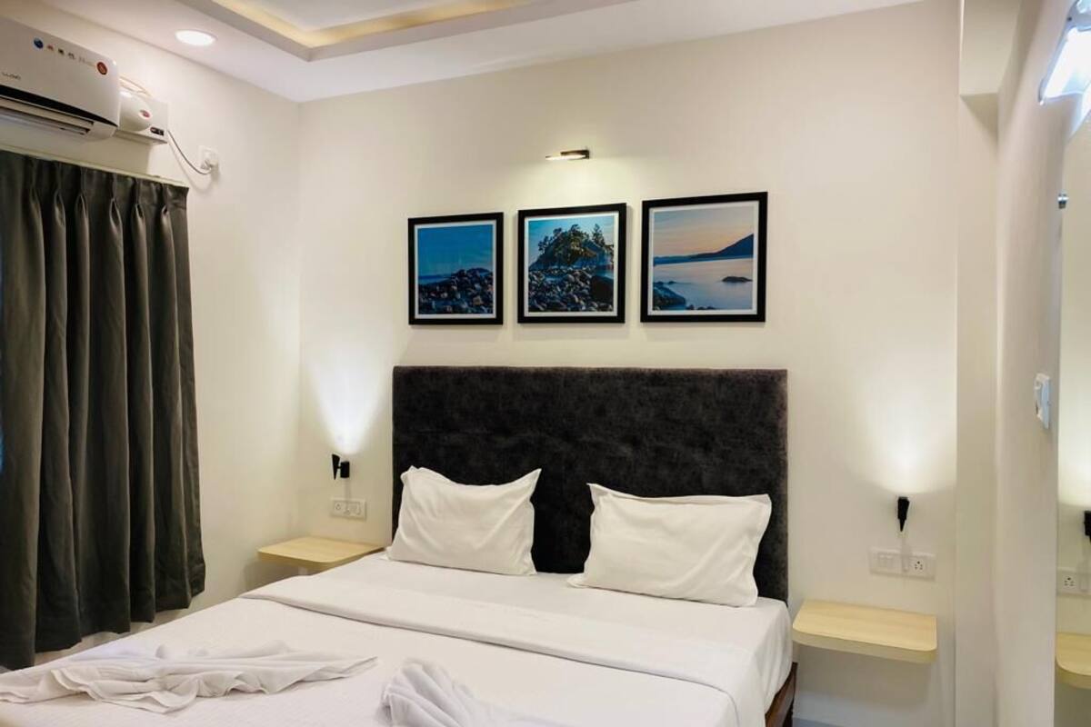 Habitación de hotel con una cama, cabecera, mesita de noche, aire acondicionado de pared y tres cuadros enmarcados.
