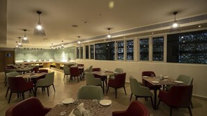 A restaurant with multiple dining tables and chairs, a bar area, and large windows with a night view.