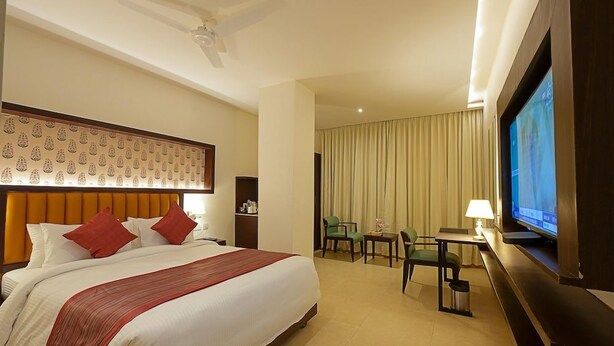 A hotel room with a large bed, a television, a desk with a chair, and a ceiling fan.