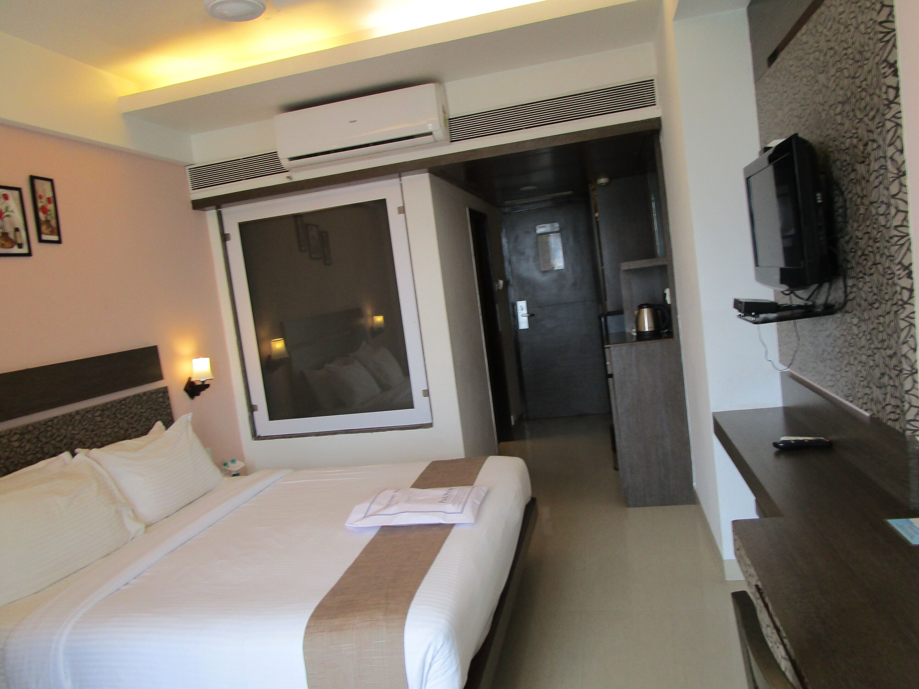 A hotel room with a bed, a TV, a desk, and a kitchenette.