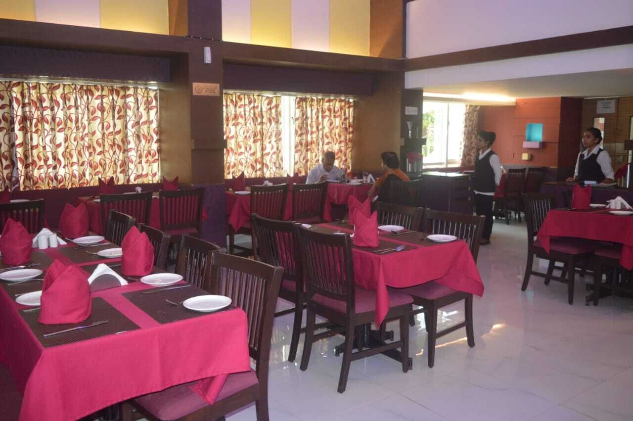 A restaurant with tables set with red tablecloths and napkins, wooden chairs, and a warm interior ambiance.