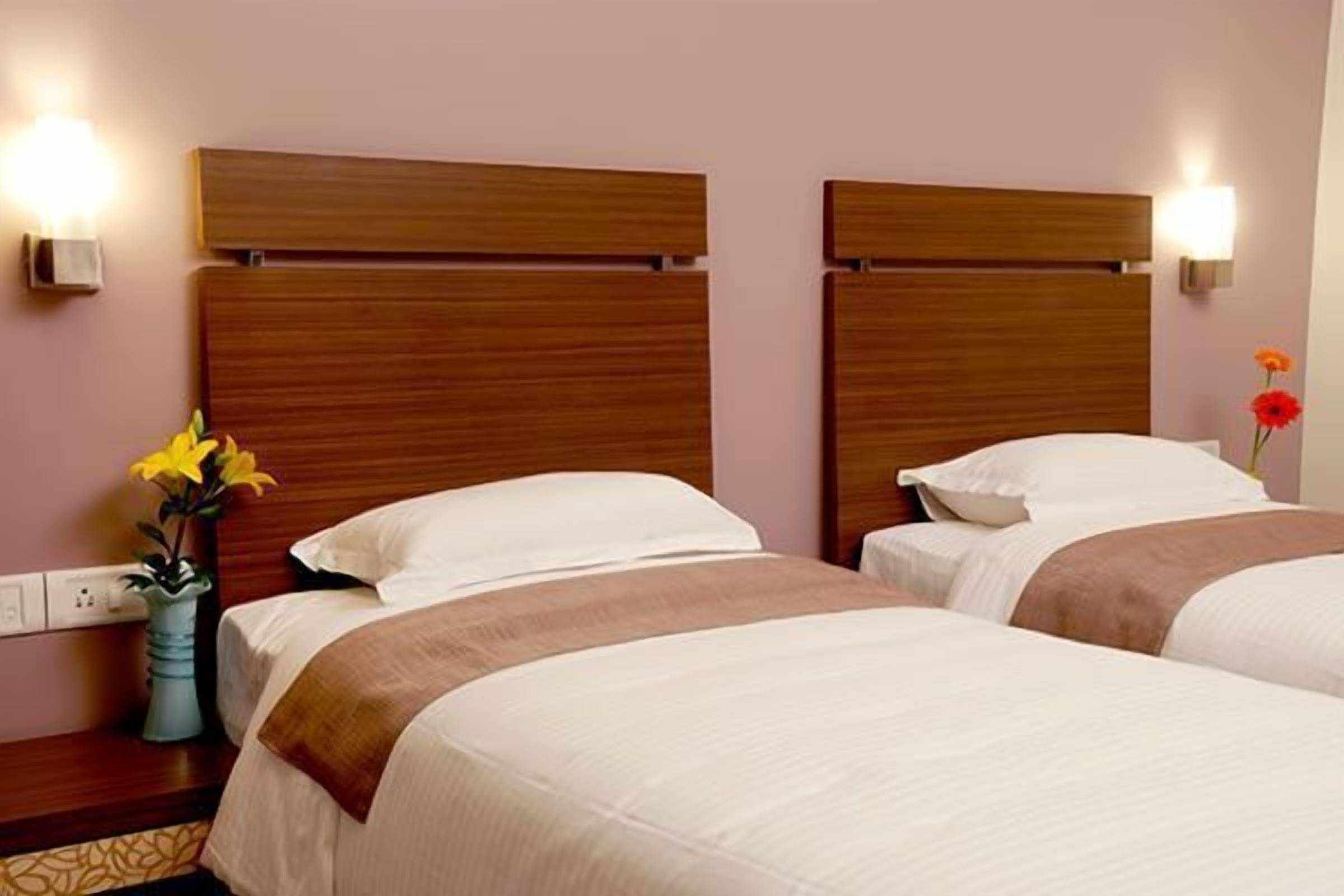 Une chambre d’hôtel avec deux lits, des têtes de lit en bois, des lampes de chevet et un vase avec des fleurs.
