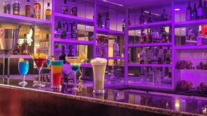 Een bar met flessen drank en diverse kleurrijke cocktails op de toonbank.
