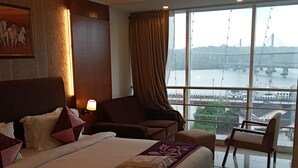Een hotelkamer met een groot bed, een bureau, een stoel en uitzicht op een brug over het water.