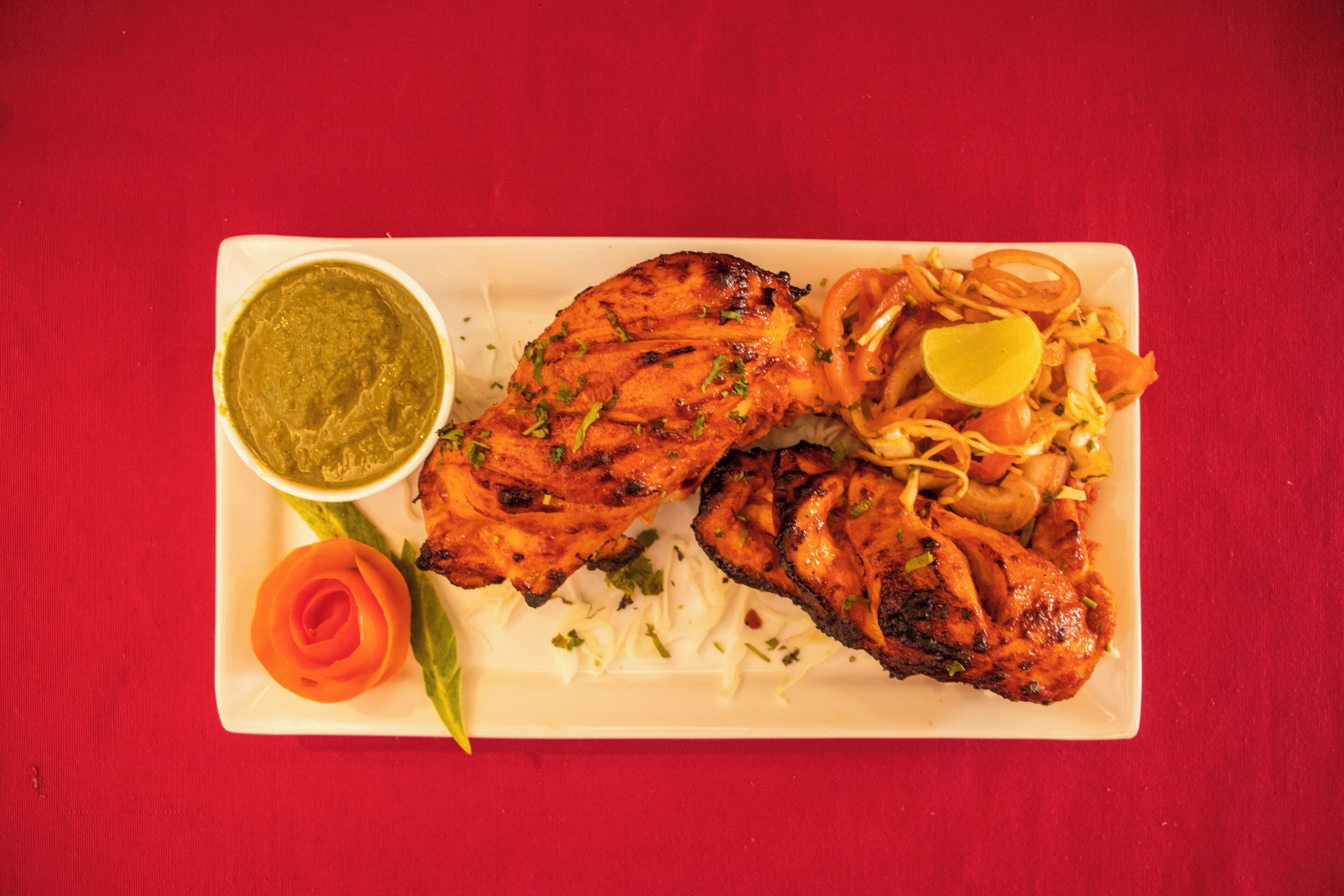 Un plato de pollo a la parrilla acompañado de arroz, verduras y salsa verde.